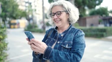 Middle age woman with grey hair using smartphone at park