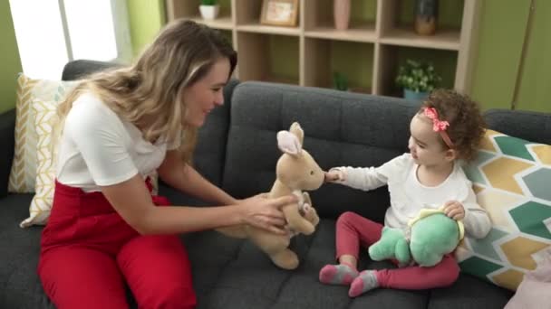 女性と幼児遊びます人形とともにソファに家に座って — ストック動画