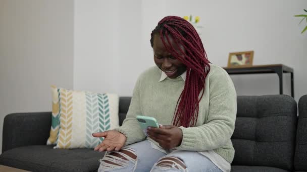 自宅で怒っているスマートフォンを使用して編組髪を持つアフリカの女性 — ストック動画