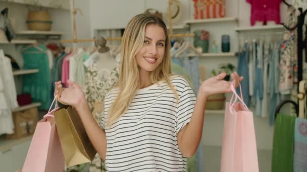 Jonge Blonde Vrouw Klant Glimlachen Zelfverzekerde Holding Boodschappentassen Kleding Winkel — Stockvideo
