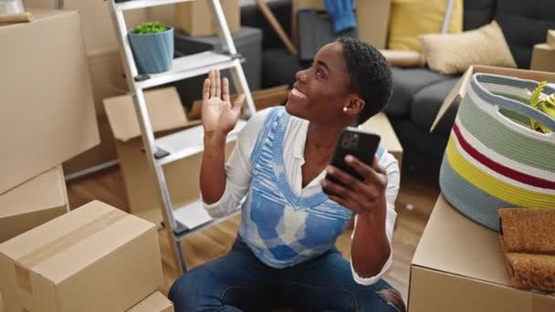 アフリカ系アメリカ人の女性がビデオ通話を持っている新しい家の床に座って — ストック動画