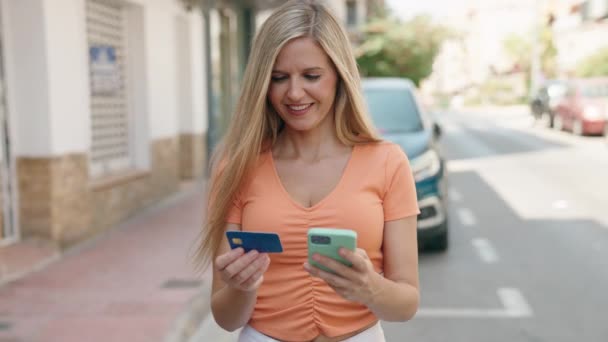 年轻的金发女人在街上用智能手机和信用卡 — 图库视频影像