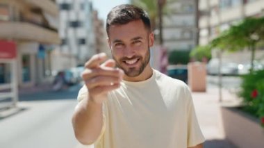 Young hispanic man smiling confident doing coming gesture with hand at street