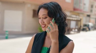 Genç, güzel, İspanyol bir kadın gülümsüyor ve caddede akıllı telefondan konuşuyor.