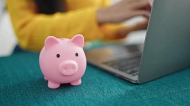 Genç ve güzel İspanyol kadın evdeki bilgisayarı kullanarak kumbaraya para sokuyor.