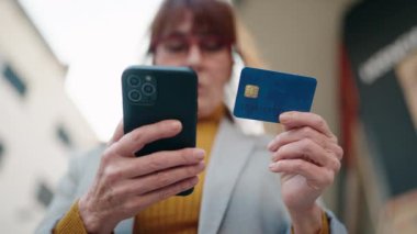 Middle age woman business executive using smartphone and credit card at street