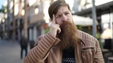 Young redhead man standing with doubt expression at coffee shop terrace