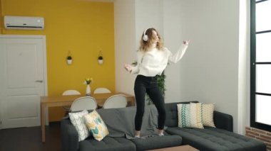 Genç sarışın kadın kanepede oturmuş evde dans eden müzik dinliyor.
