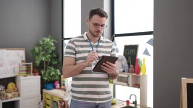 Anaokulunda tabletle öğretmen olarak çalışan genç beyaz bir adam.