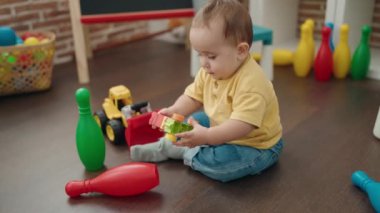 Adorable hispanic baby playing with construction blocks sitting on floor at kindergarten