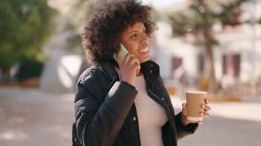 Genç Afrikalı Amerikalı kadın akıllı telefondan konuşuyor parkta kahve içiyor.