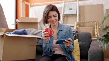 Beyaz kadın akıllı telefon kullanıyor. Yeni evinde kahve içiyor.