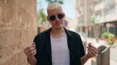 Genç beyaz adam kendine gülerek para harcıyor sokakta jest yapıyor.