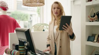 Elbise mağazasında çalışan genç sarışın kadın mağaza asistanı dokunmatik ped kullanıyor.