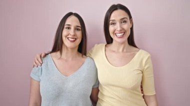 İzole edilmiş pembe arka planda birbirlerine sarılarak gülümseyen iki kadın.
