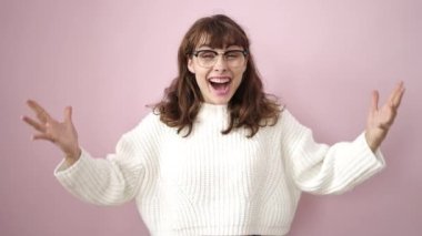 Young caucasian woman standing with surprise expression and raised arms over isolated pink background