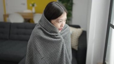 Young chinese woman covering with blanket for cold sitting on sofa at home