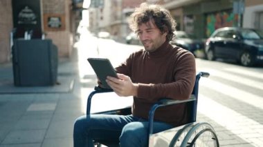 Young hispanic man using touchpad sitting on wheelchair at street