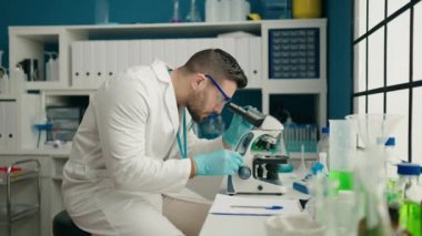 Laboratuardaki belgeye mikroskop kullanarak bilim adamı üniforması giyen İspanyol genç adam.