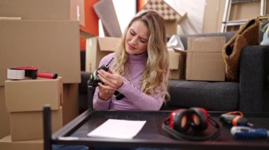 Genç sarışın kadın yeni evinde endişeli bir ifadeyle masayı onarıyor.