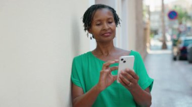 Middle age african american woman smiling confident using smartphone at street