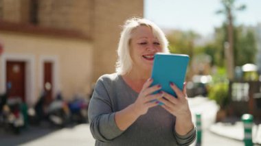 Middle age blonde woman smiling confident having video call at street