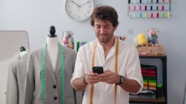 Genç İspanyol terzi, elbise fabrikasında akıllı telefon kullanarak gülümsüyor.