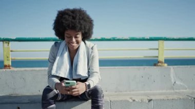 African american woman wearing sportswear using smartphone at seaside