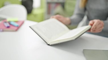 Kitap okuyan beyaz bir kadın kütüphane üniversitesinde masada oturuyor.