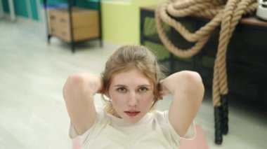 Young blonde woman lying on yoga mat training abs exercise at sport center