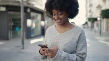 Afro-Amerikalı kadın sokakta akıllı telefon kullanarak kendine güveniyor.
