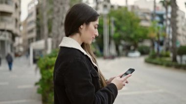 Parkta akıllı telefon kullanarak gülümseyen güzel bir İspanyol kadın.