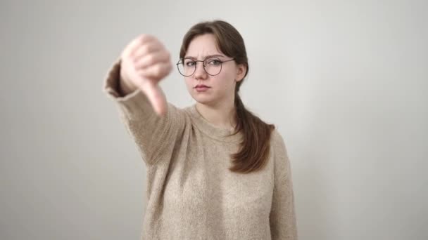 年轻的金发女子用大拇指低垂在孤立的白色背景下做着消极的手势 — 图库视频影像