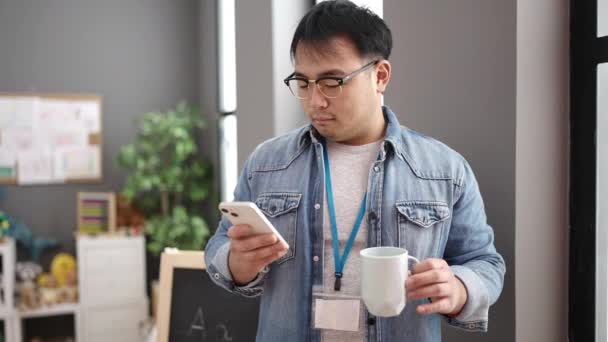 Young Chinese Man Preschool Teacher Using Smartphone Drinking Coffee Kindergarten — Stock video