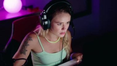 Genç sarışın kadın oyun odasında bilgisayar kullanarak video oyunu oynuyor.