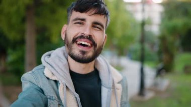 Genç İspanyol adam gülümsüyor. Parkta kendine güvenen bir video çağrısı var.