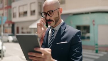 Latin asıllı genç bir yönetici akıllı telefondan konuşuyor. Sokakta dokunmatik ped kullanıyor.