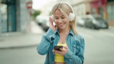 Young blonde woman smiling confident listening to music and dancing at street