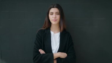 Genç İspanyol kız gülümsüyor. Kollarını kavuşturup siyah arka planda duruyor.