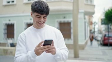 Genç İspanyol adam sokakta gülümseyen akıllı telefon kullanıyor.