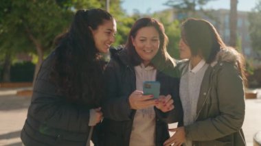 Mother and daughters smiling confident using smartphone at park