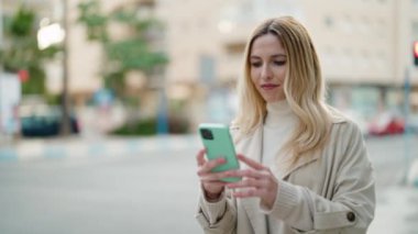 Young blonde woman smiling confident making selfie by the smartphone at street