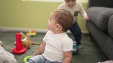 Evde yerde oturmuş oyuncaklarla oynayan iki sevimli bebek.