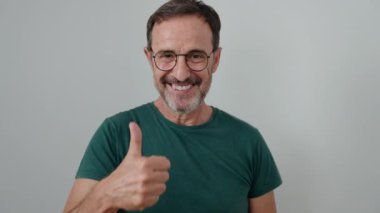 Orta yaşlı bir adam kendinden emin gülümsüyor. İzole edilmiş beyaz arka plan üzerinde baş parmağıyla imza atıyor.