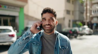 Genç Arap adam gülümsüyor, kendinden emin bir şekilde caddedeki akıllı telefondan konuşuyor.