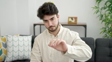 Kanepede oturan İspanyol asıllı genç adam ciddi bir ifadeyle evde jest yapıyor.