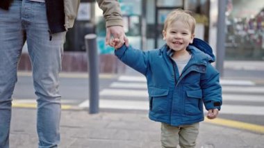 Beyaz çocuk sokakta babamla el ele tutuşurken gülümsüyor.