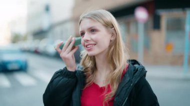 Young blonde girl smiling confident listening audio message by the smartphone at street
