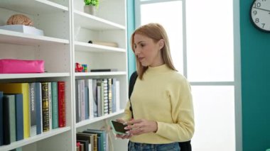 Üniversite sınıfında akıllı telefon kullanarak kitap arayan genç sarışın kız öğrenci.