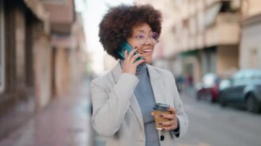 Afro-Amerikalı kadın akıllı telefonda konuşuyor. Sokakta kahve içiyor.